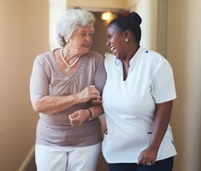 Caregiver providing companionship to elderly woman as they laugh together.