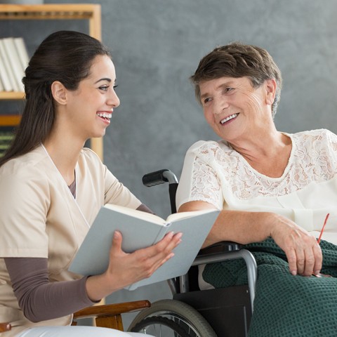 Client and caregiver enjoy each other's company as they read a book together.