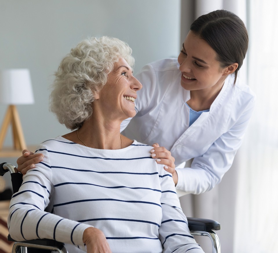 Elderly woman in wheelchair smiling at young caregiver as she receives in-home care.