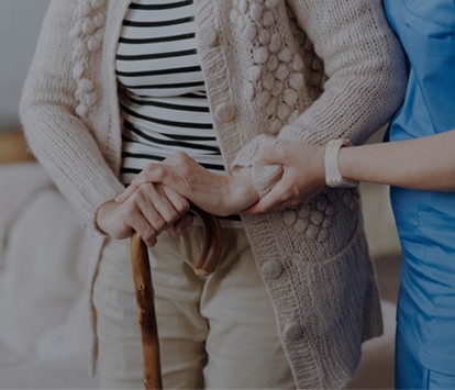 Cropped image focusing on caregiver assisting elderly woman with cane.