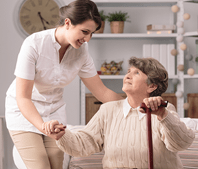 Home Care Helper Aids Woman Sitting Down With a Walking Stick