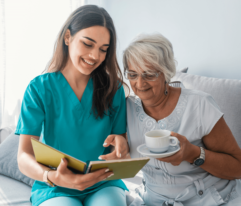 Home Care Professional Sitting on Bed Reading with Elderly Woman