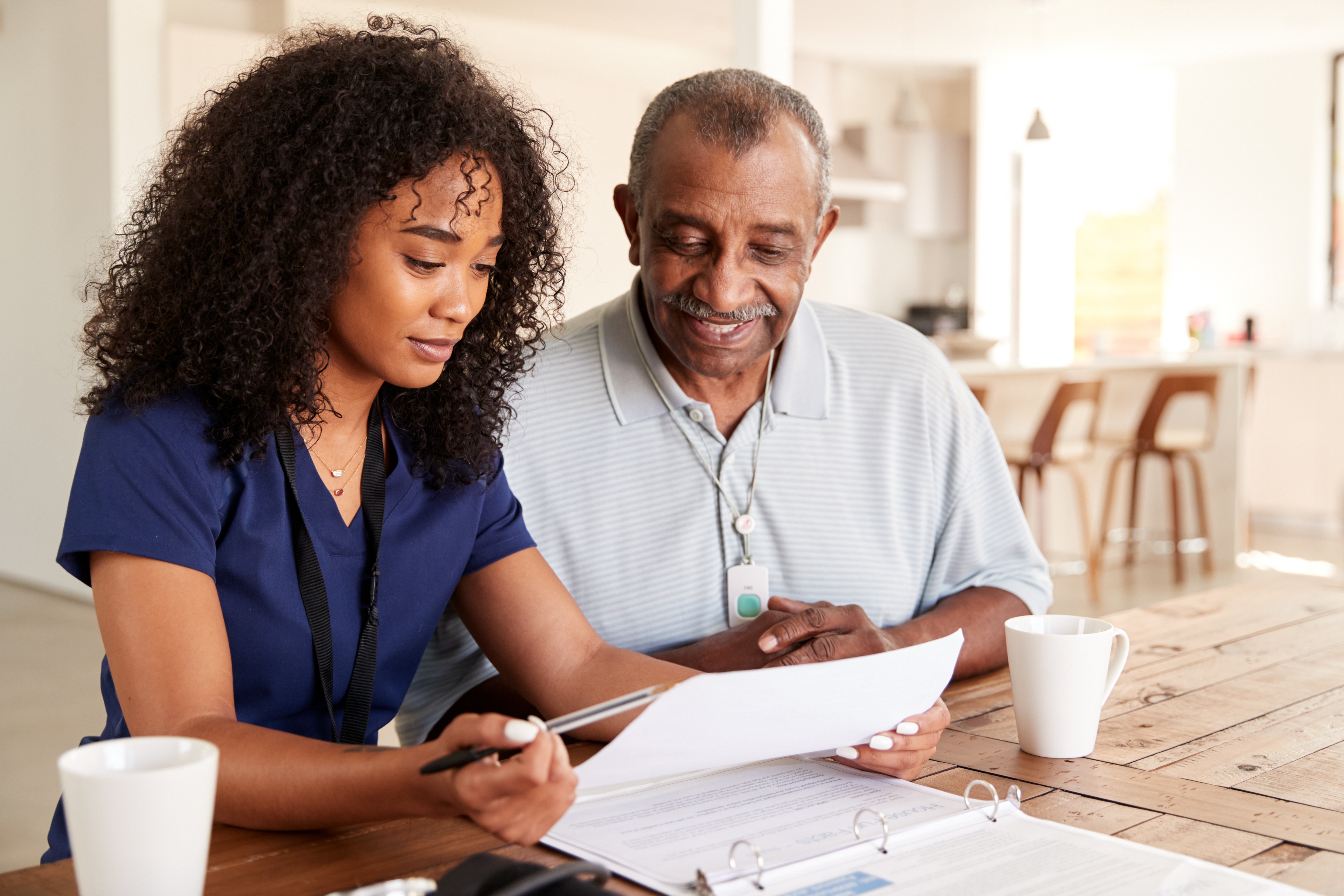 Female caregiver checking test results with a senior man during a home care visit.