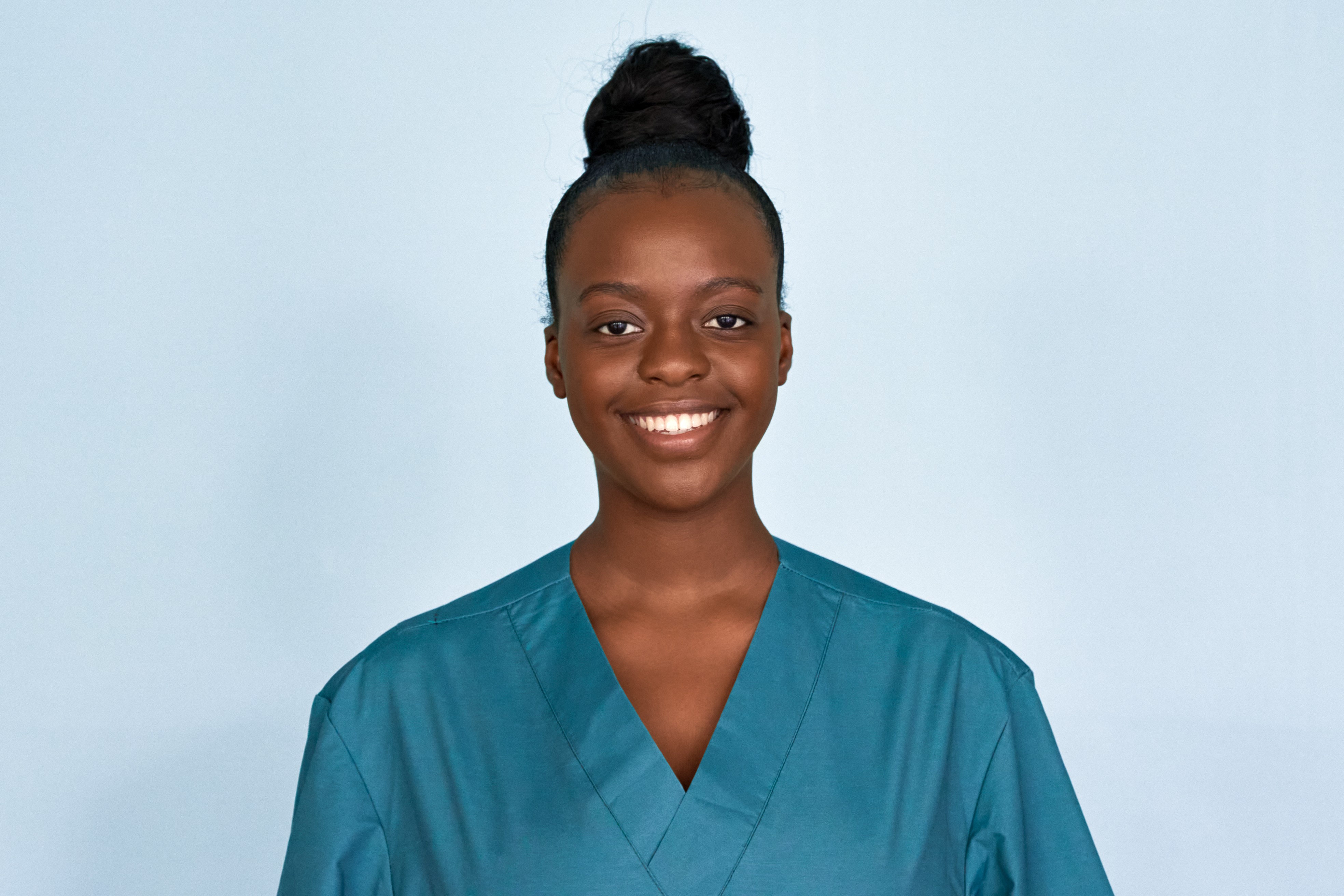 A female private duty aide wearing teal scrubs smiles at camera.