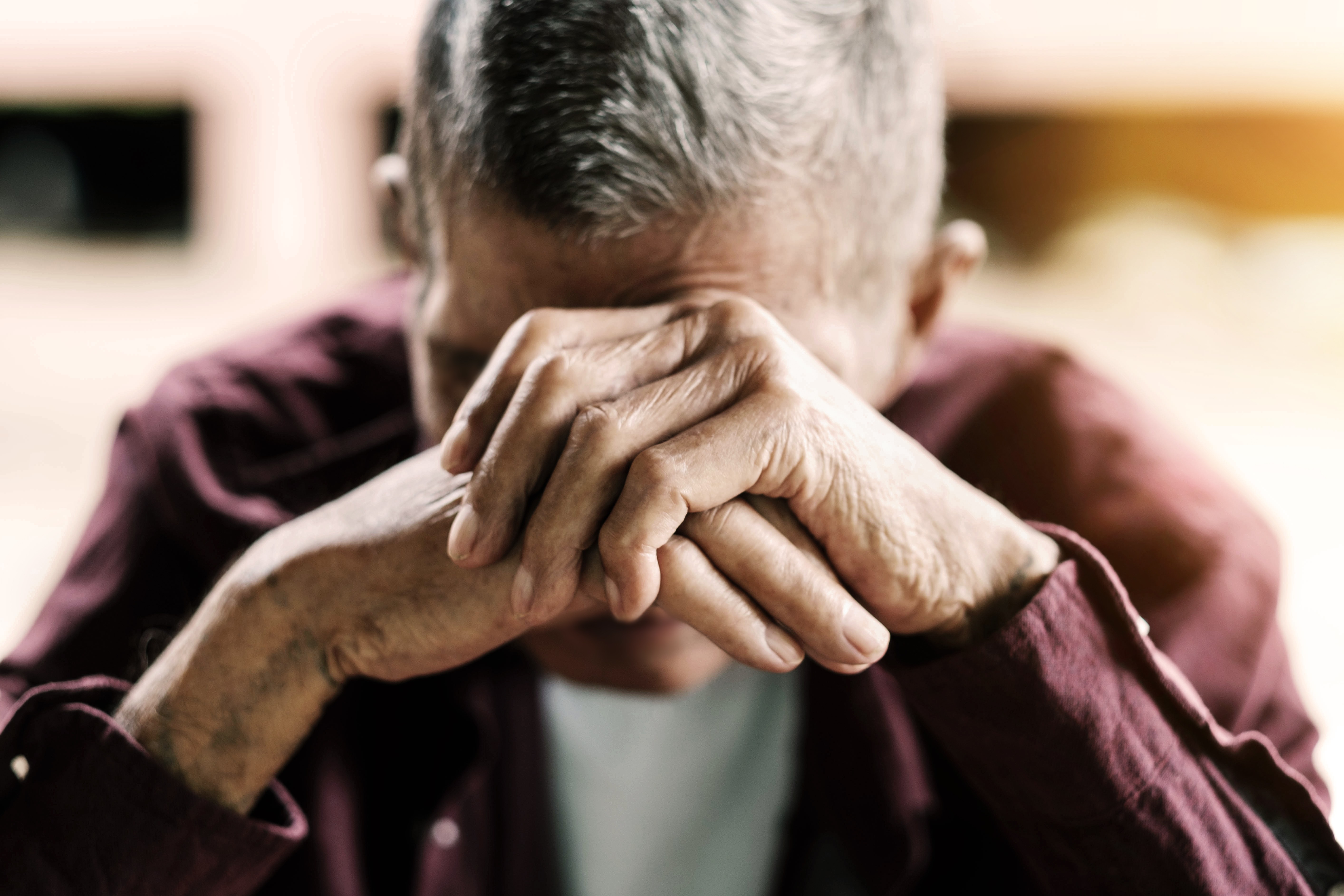 Senior man covers his face with his hands due to loneliness and isolation.