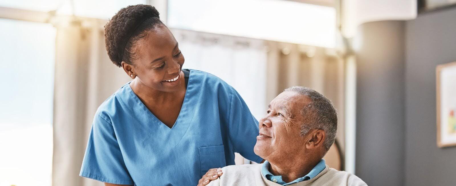 Elderly man in wheelchair smiles at his Medicare home health care caregiver.
